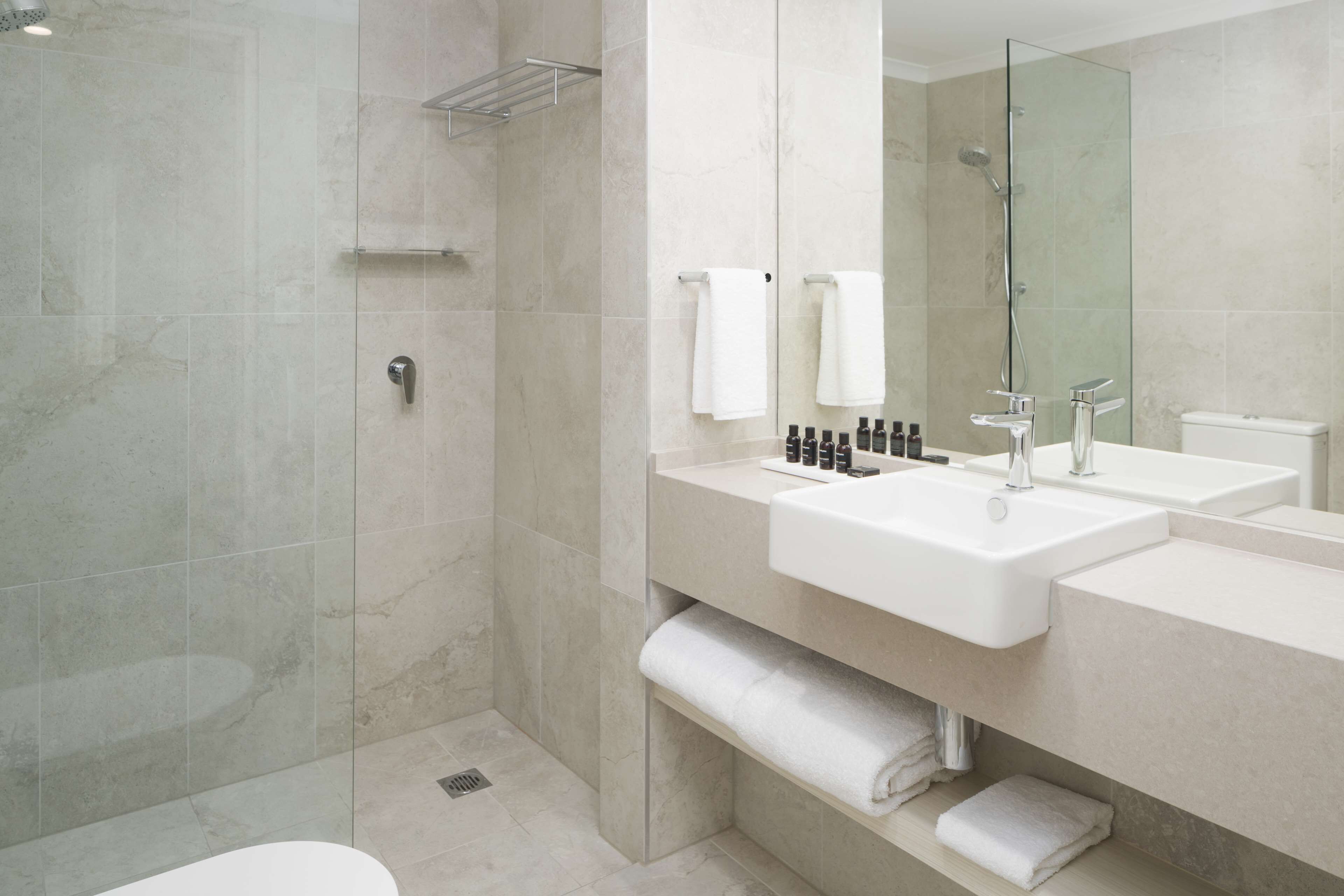 Une salle de bain moderne dotée d’une douche à parois de verre, d’un grand miroir et d’un meuble-lavabo avec un évier et un porte-serviettes.
