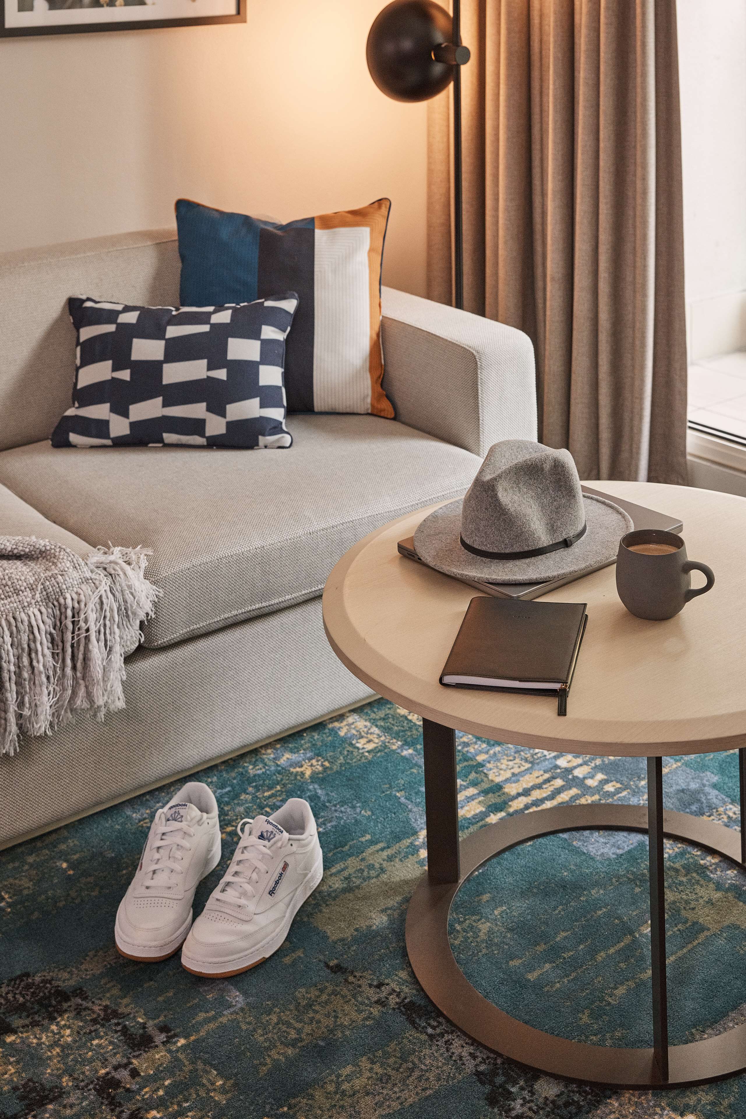 Un salon moderne avec un canapé, une table basse ronde, un chapeau, un carnet et une paire de baskets.