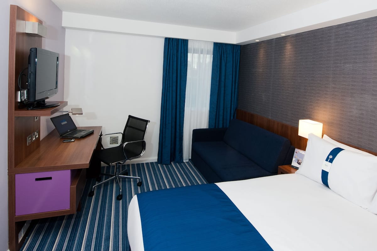 Une chambre d’hôtel comprenant un lit, un bureau avec un ordinateur portable, une chaise, une télévision et une table de chevet avec une lampe.