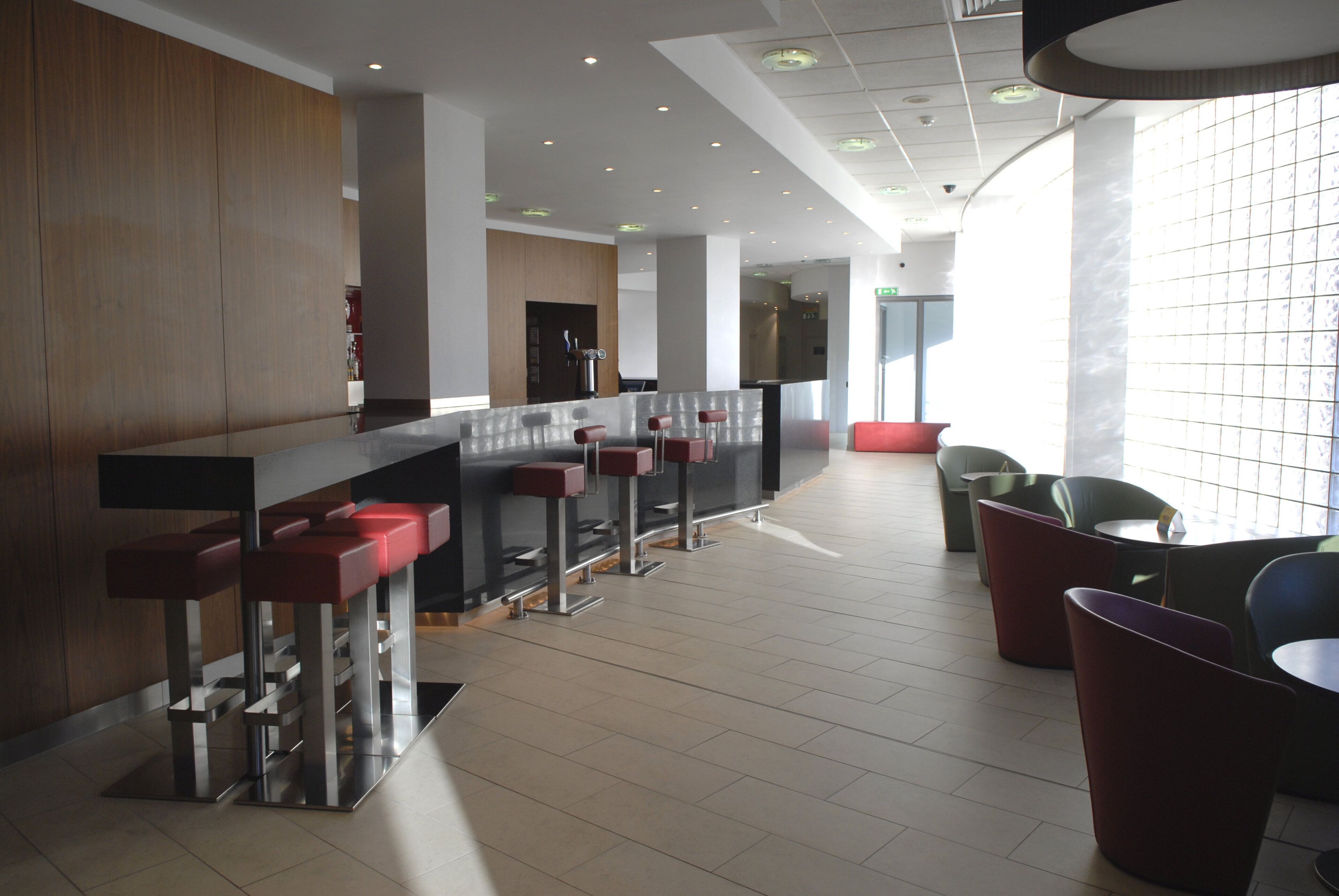 Eine moderne Bar mit einer langen Theke, mehreren Barhocker und einer Sitzecke mit Stühlen und Tischen.