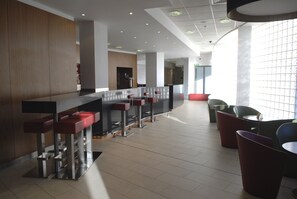 A modern bar area with a long counter, multiple stools, and a seating area with chairs and tables. - Holiday Inn Express London City by IHG (London)