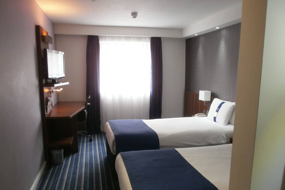 Une chambre d’hôtel avec deux lits, un bureau avec une chaise, une télévision et une fenêtre avec des rideaux.