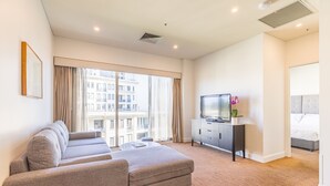 A modern hotel room with a large window, a sofa, a TV, and a bed. - Seasons Botanic Gardens (Melbourne)