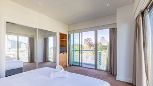 A hotel room with a large bed, a TV, a wooden cabinet, and a balcony with a city view. - Seasons Botanic Gardens (Melbourne)