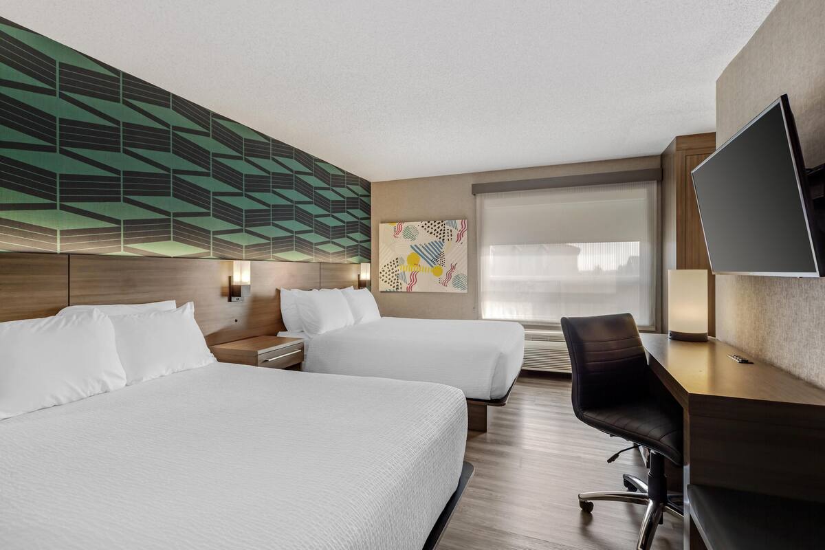 Een hotelkamer met twee bedden, een bureau, een stoel, een televisie en een groot raam.
