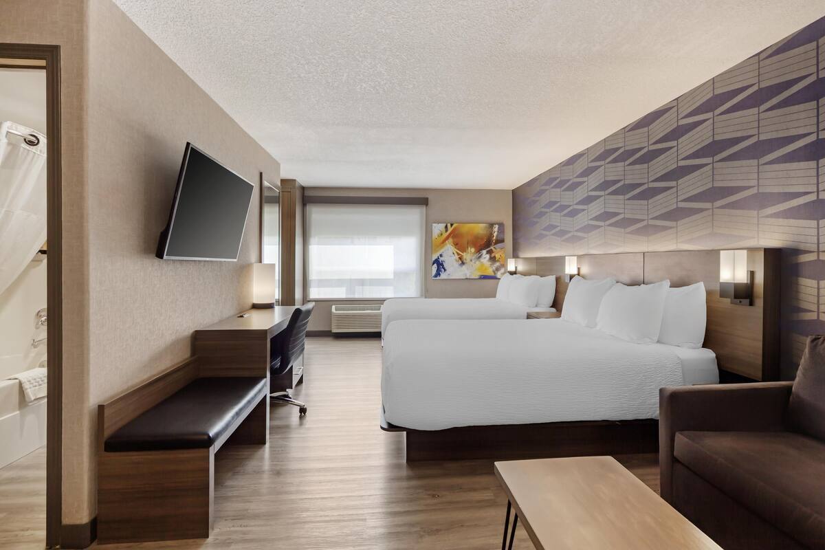 Een hotelkamer met een groot bed, een bureau, een bankje, een televisie en een muur met geometrische patronen.