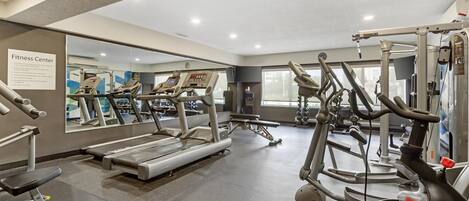 Centro de ginástica com esteiras, aparelhos elípticos e equipamentos de musculação.