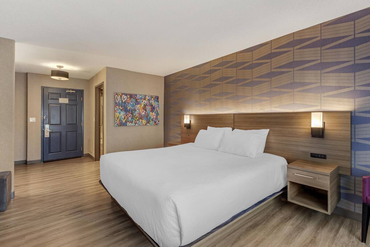 Een hotelkamer met een groot bed, een nachtkastje, een wandlamp en een deur.