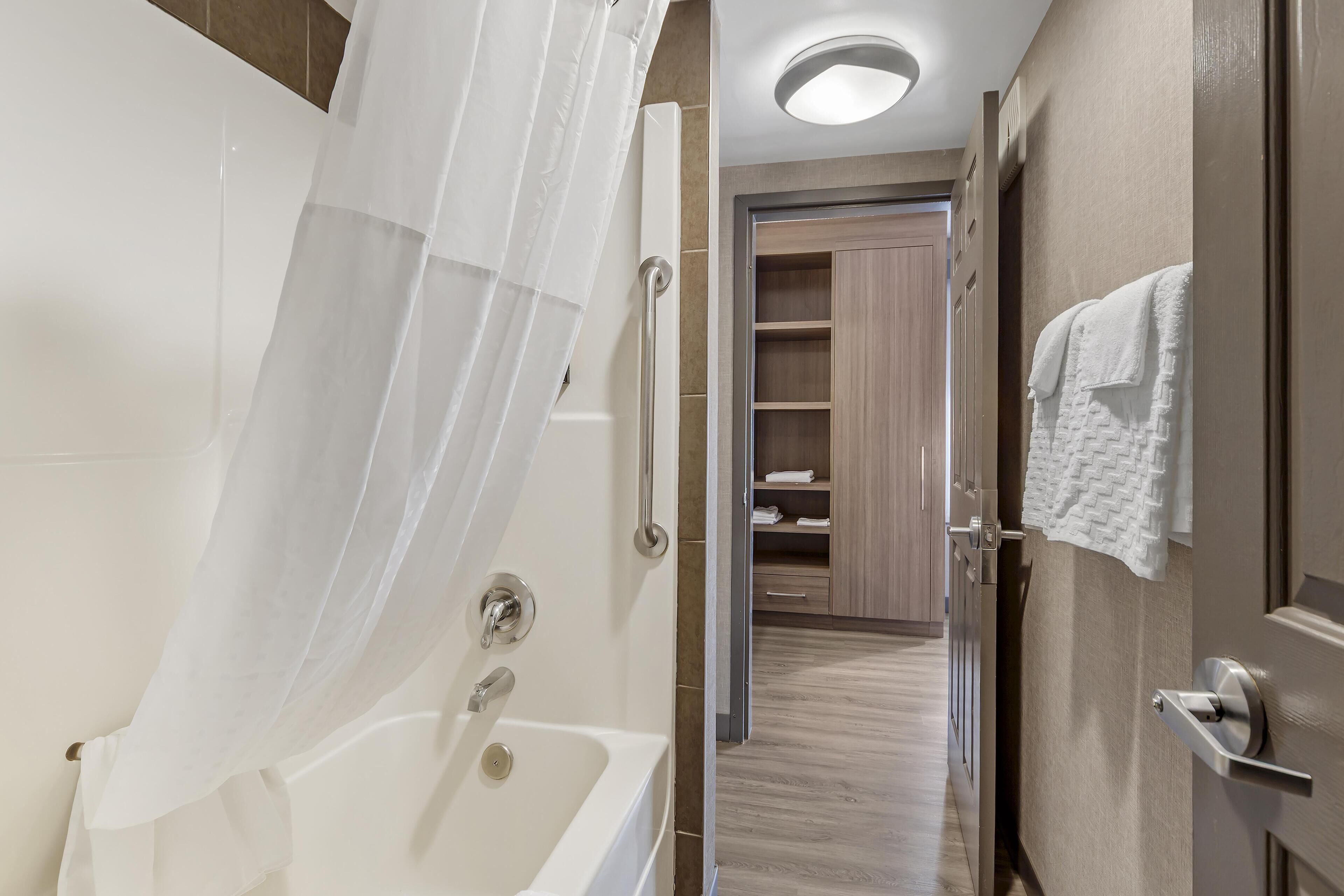 A modern bathroom with a bathtub, shower curtain, and wooden shelving.