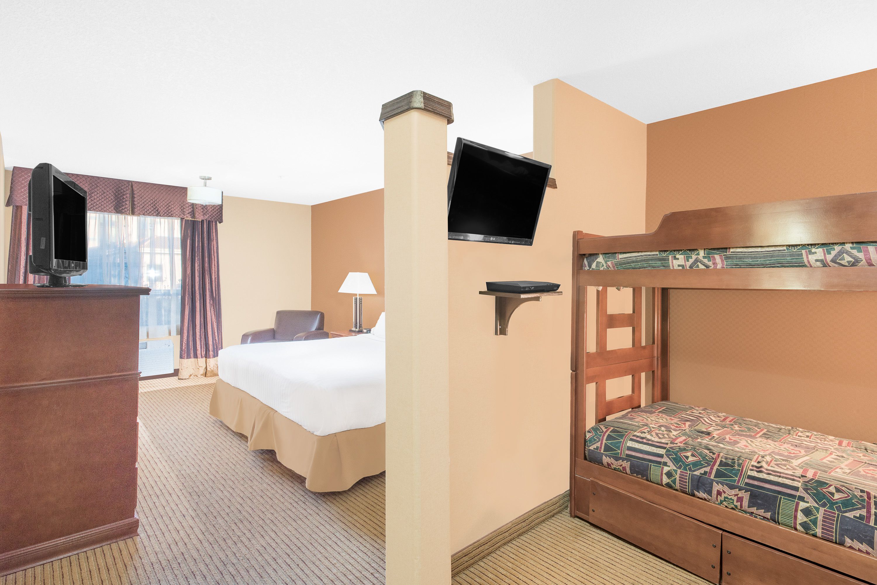 A hotel room with a bed, a desk, a television mounted on the wall, and a bunk bed.