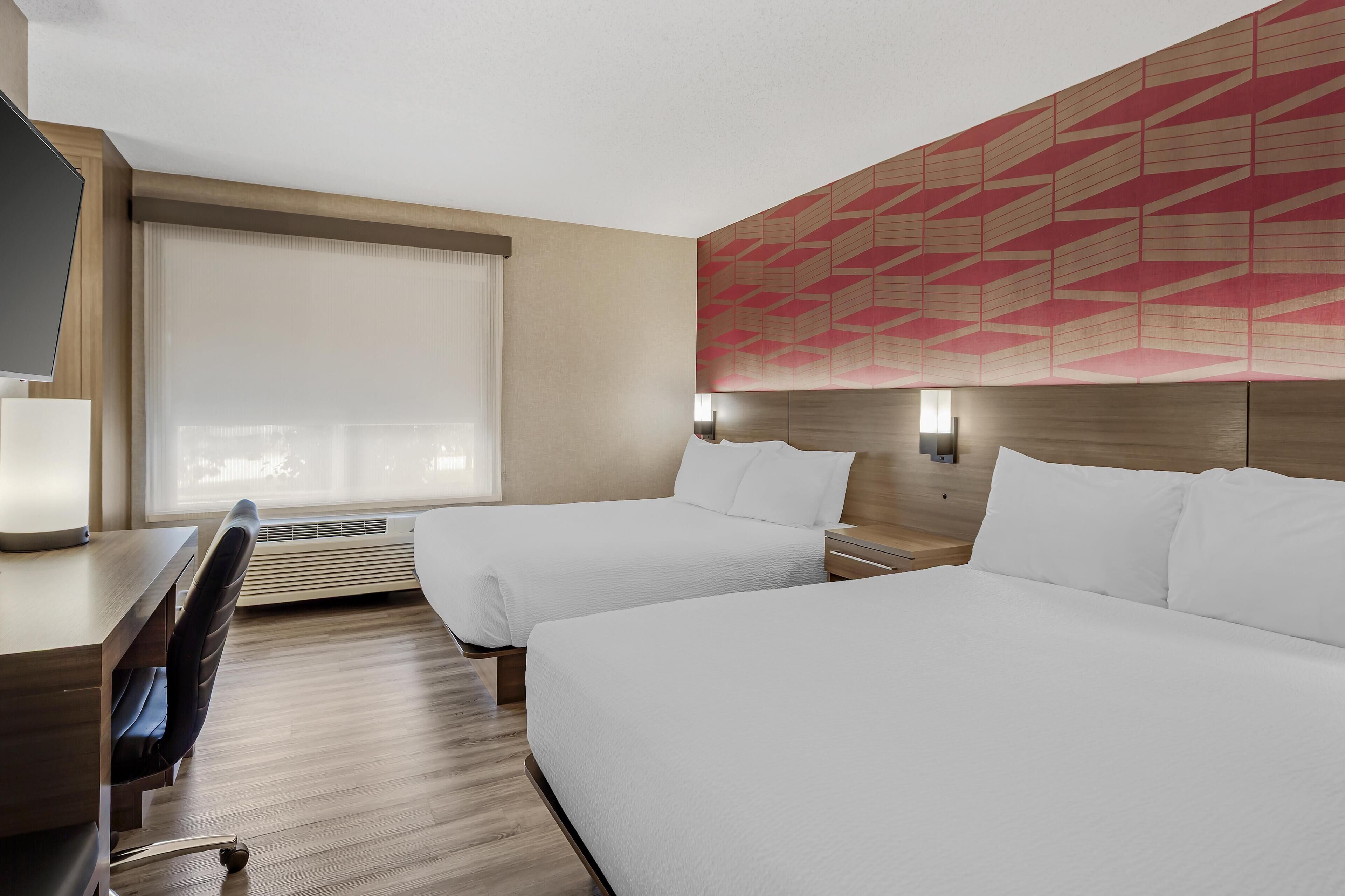A hotel room with two beds, a desk, and a chair.
