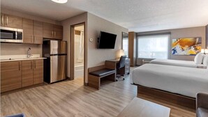 Une chambre d’hôtel moderne équipée d’une kitchenette, d’un téléviseur à écran plat, d’un lit et d’un bureau avec une chaise.
