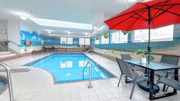 Una piscina interior con suelo de baldosas, una sombrilla roja y un mural que representa una playa.
