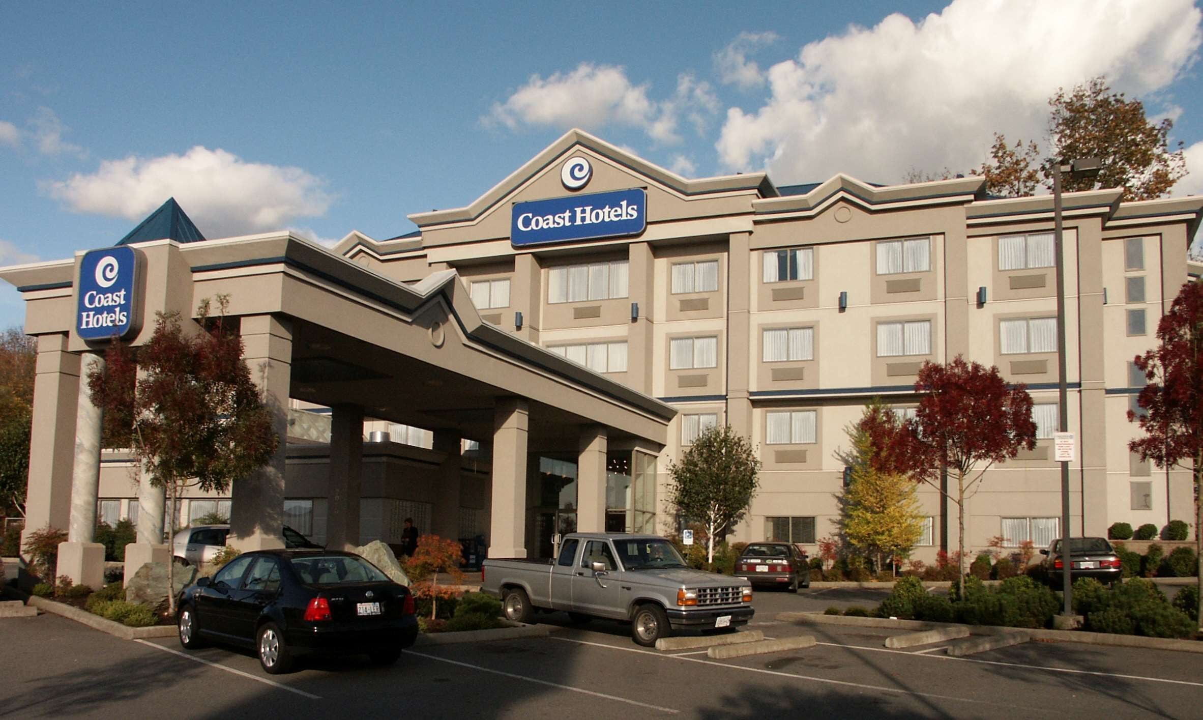 A hotel with a prominent sign, a covered entrance, and a parking lot with vehicles.