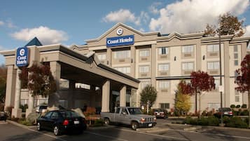 A hotel with a prominent sign, a covered entrance, and a parking lot with vehicles.
