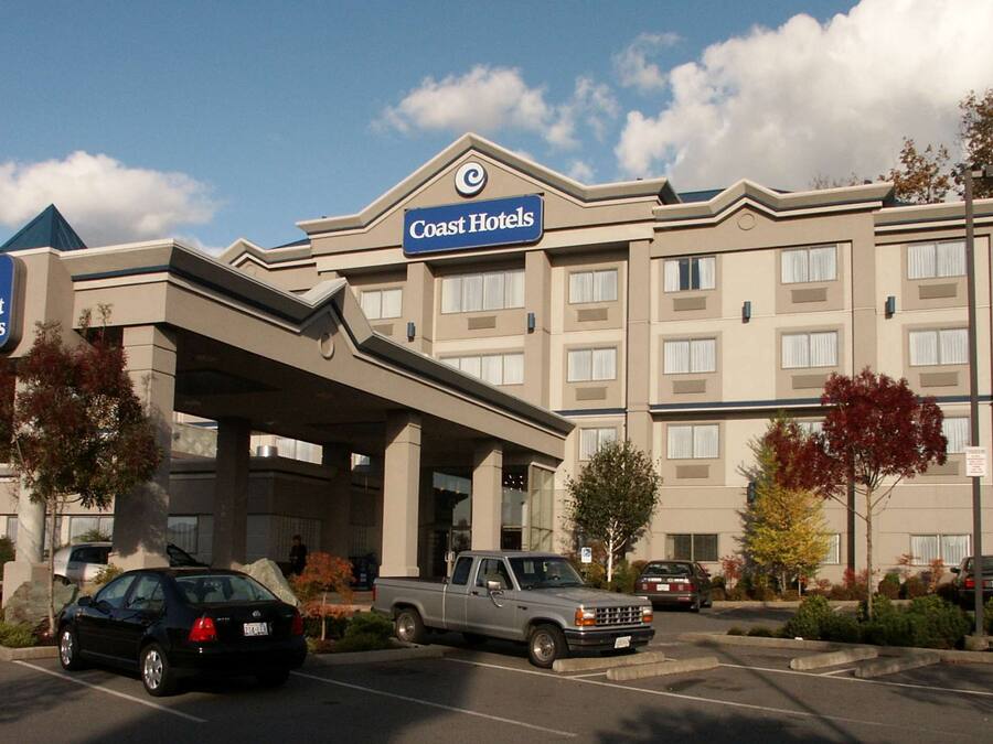 A hotel with a prominent sign, a covered entrance, and a parking lot with vehicles.