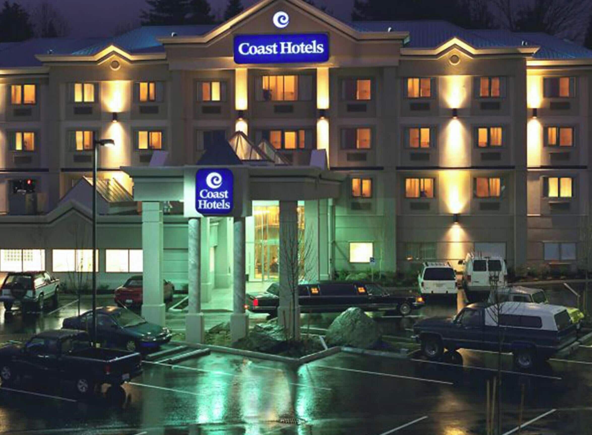 A large hotel with multiple floors, a prominent sign, and a parking lot with several vehicles.