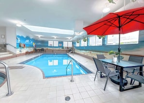 An indoor swimming pool with a tiled floor, a red umbrella, and a mural depicting a beach scene.
