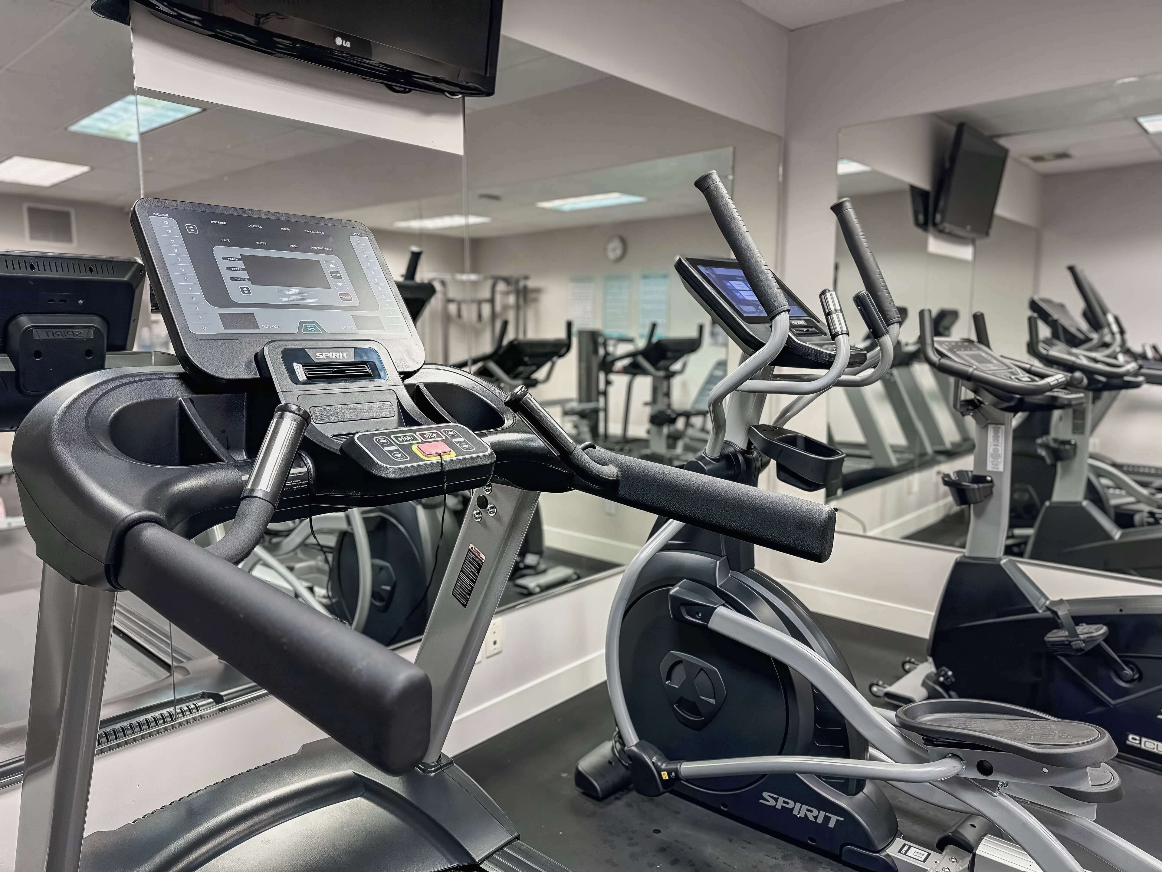 Ein Fitnessraum mit mehreren Laufbändern, einer Bedienkonsole und einer Spiegelwand.