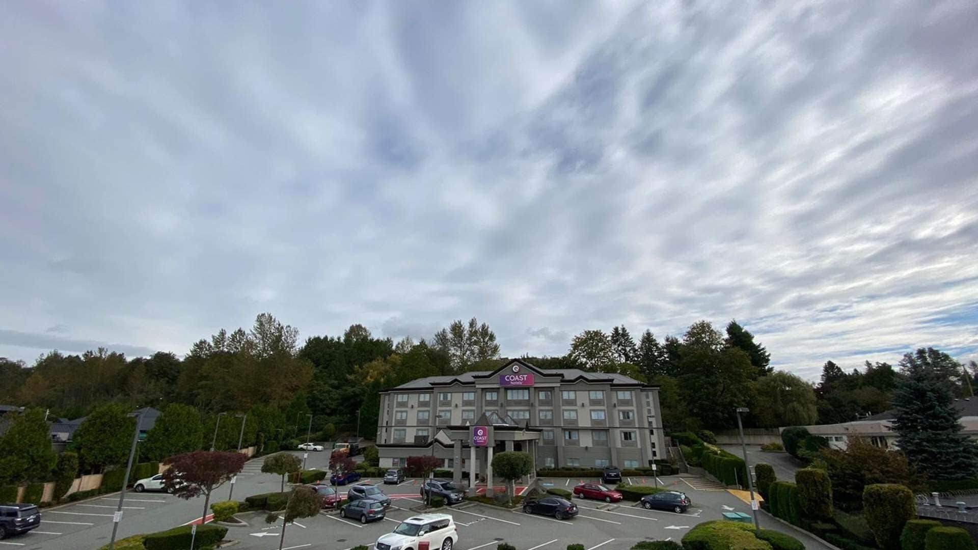 A hotel with a parking lot, surrounded by trees and a cloudy sky.