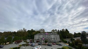 A hotel with a parking lot, surrounded by trees and a cloudy sky.