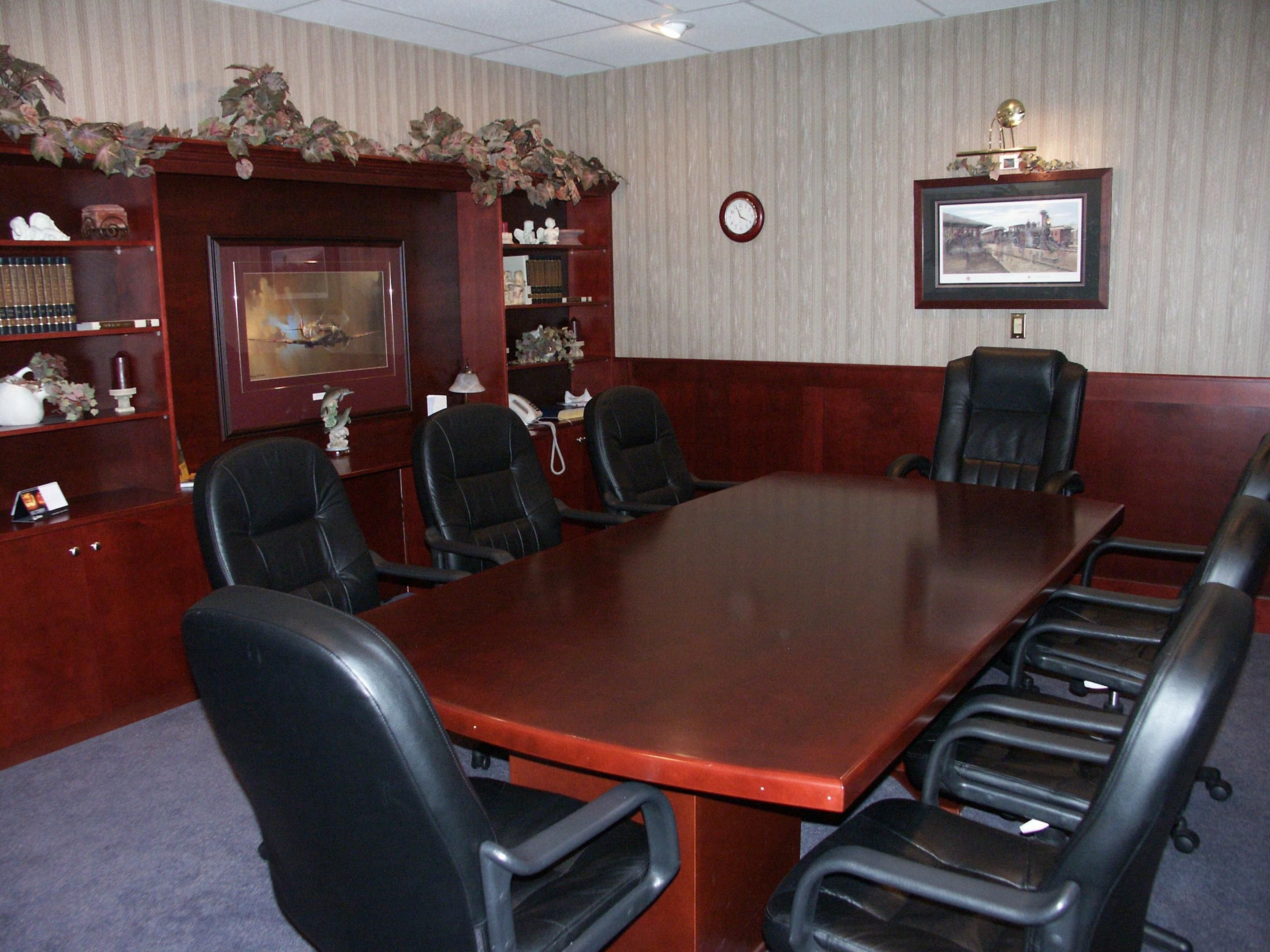 A conference room with a large wooden table, black leather chairs, a clock, and framed pictures on the walls.