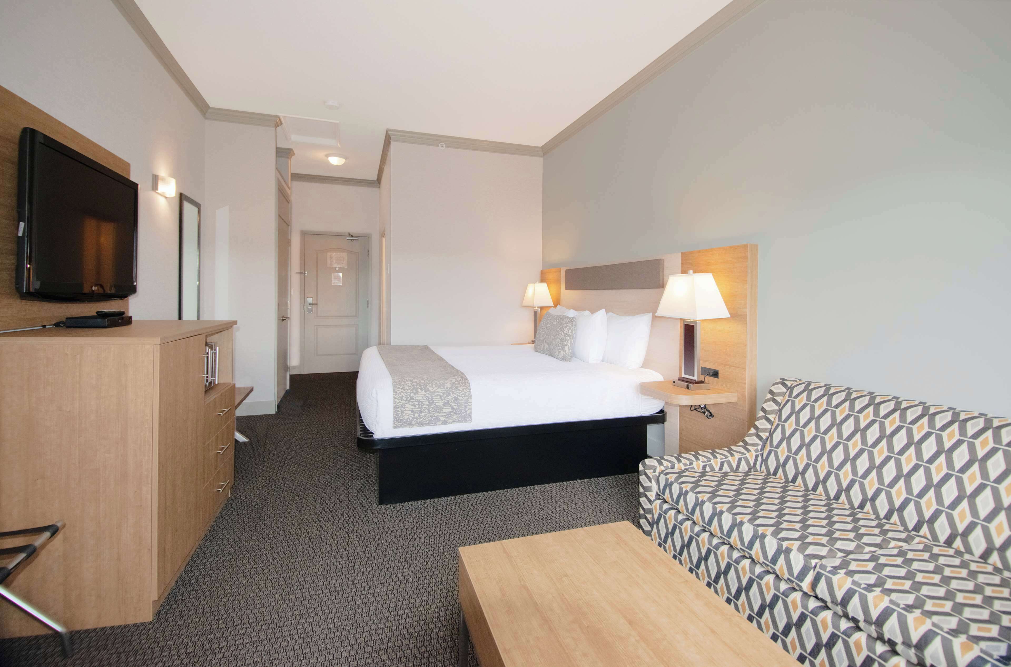 A hotel room with a bed, a TV, a desk, a sofa, and a lamp.