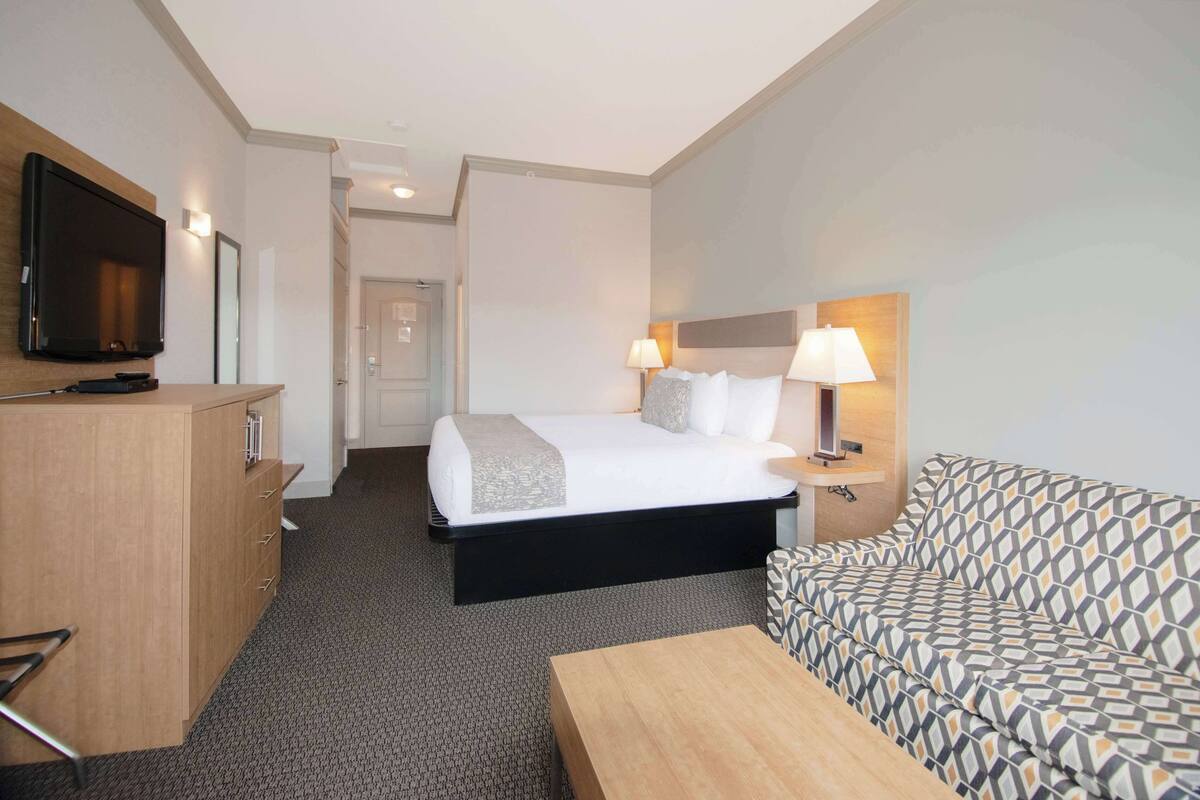 Ein Hotelzimmer mit Bett, Fernseher, Schreibtisch, Sofa und Lampe.