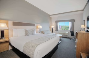 Une chambre d’hôtel avec un grand lit, des tables de chevet, un bureau, une chaise, une télévision et une fenêtre donnant sur un beau paysage.