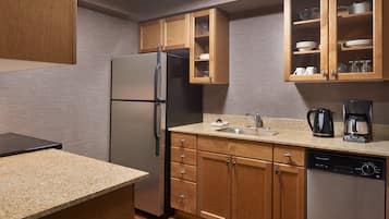 A compact kitchen with wooden cabinets, a stainless steel refrigerator, a dishwasher, and a coffee maker.