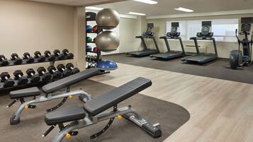 Une salle de sport équipée de tapis de course, de bancs de musculation et de ballons d’exercice.