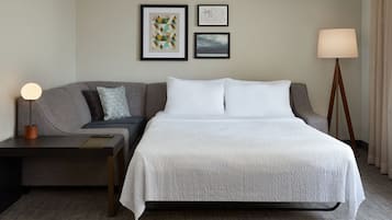 A hotel room with a bed, a sofa, a lamp, and framed pictures on the wall.