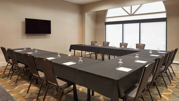 Un salón de conferencias con una mesa larga, sillas, un televisor de pantalla plana y ventanas amplias.