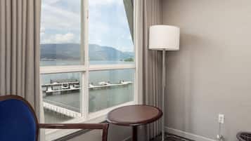 Une chambre d’hôtel dotée d’une grande fenêtre donnant sur un port de plaisance et des bateaux. On y trouve une table ronde et une chaise bleue.
