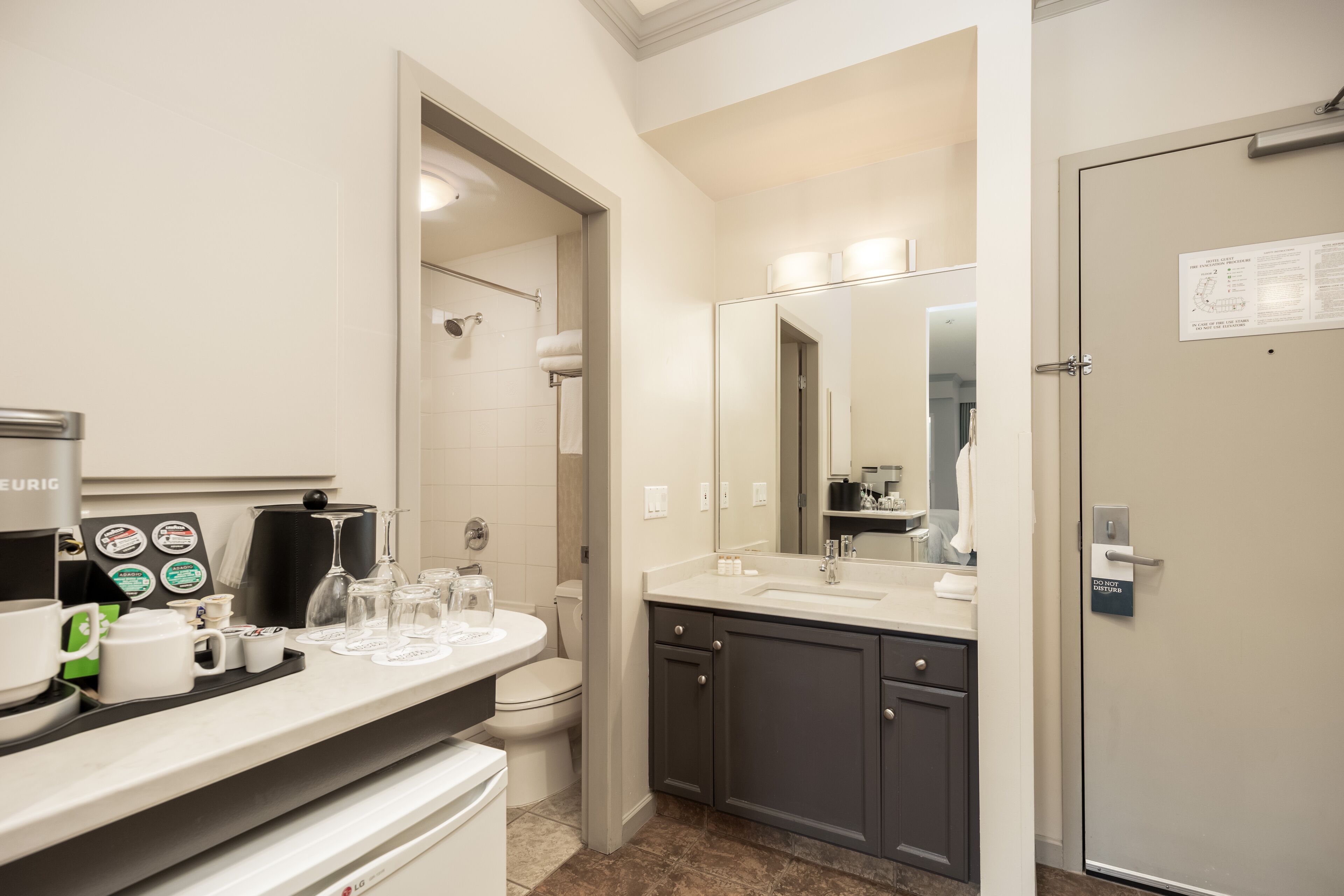 A modern bathroom with a coffee station, a large mirror, and a door with a sign.