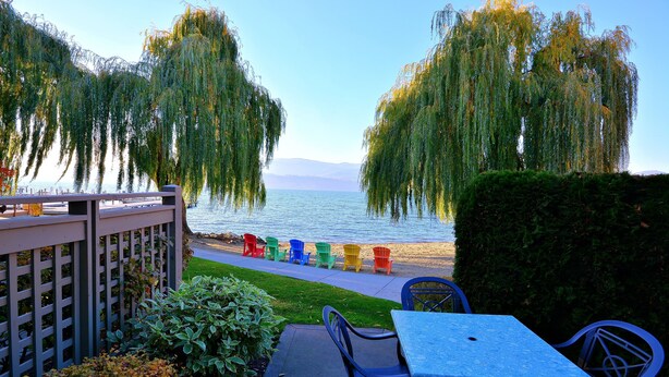 Un patio junto al lago con vistas al agua, una terraza de madera y sillas Adirondack de colores.