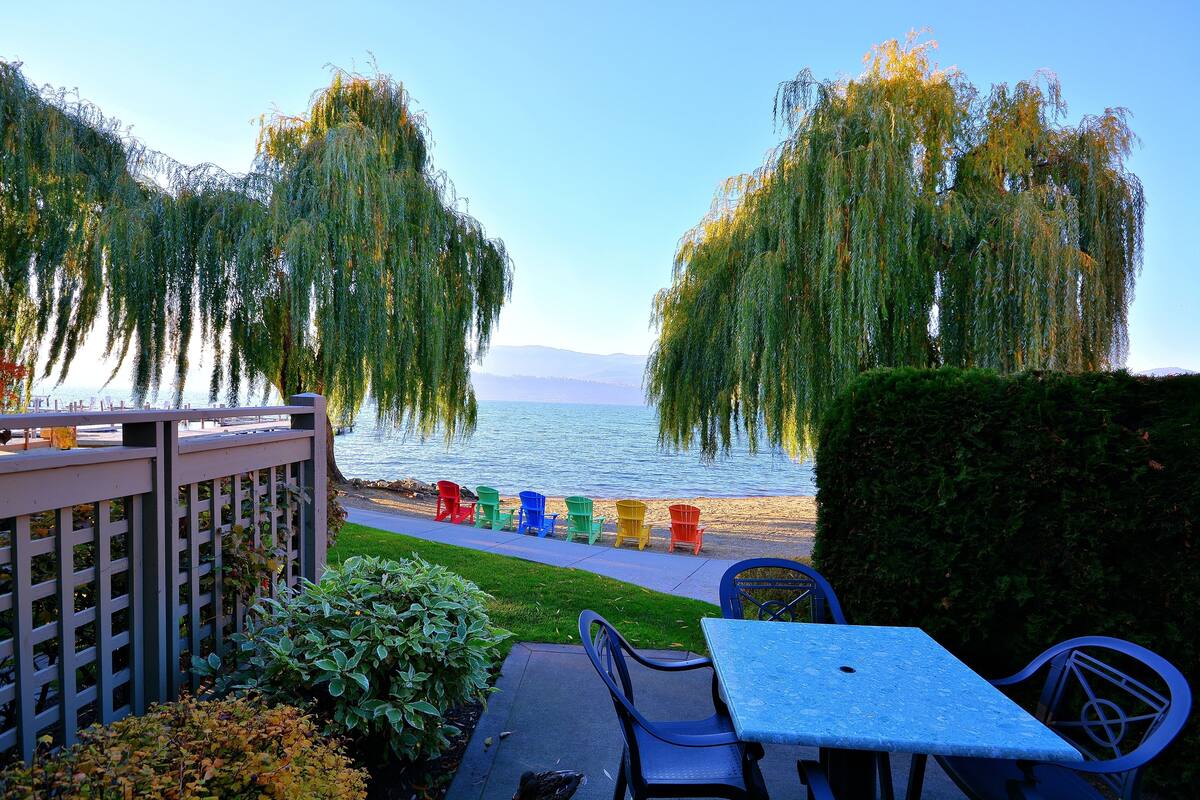 Un patio junto al lago con vistas al agua, una terraza de madera y sillas Adirondack de colores.
