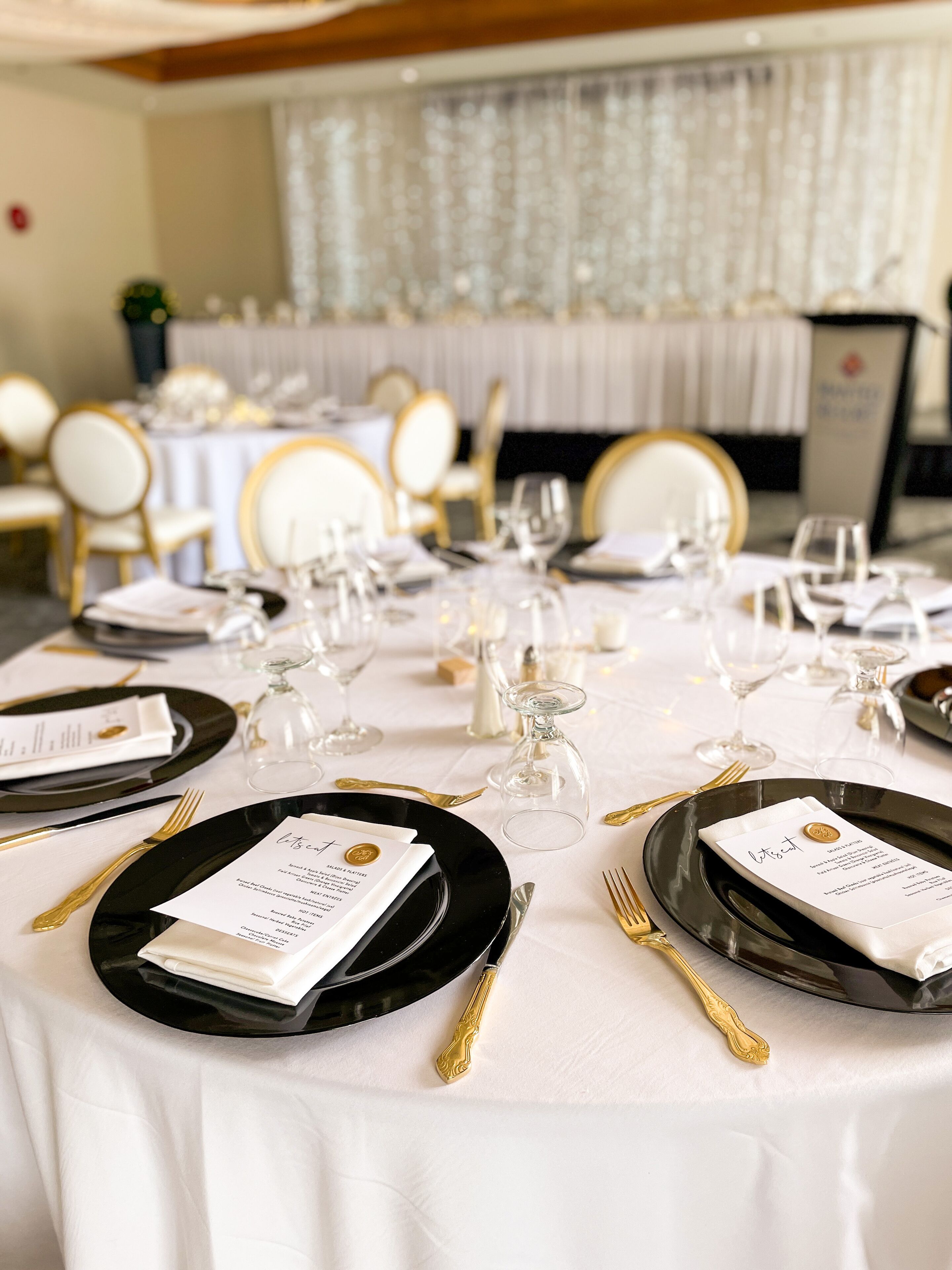 Een feesttafel gedekt met zwarte borden, gouden bestek en heldere wijnglazen, met menukaarten bij elk zitplaats.