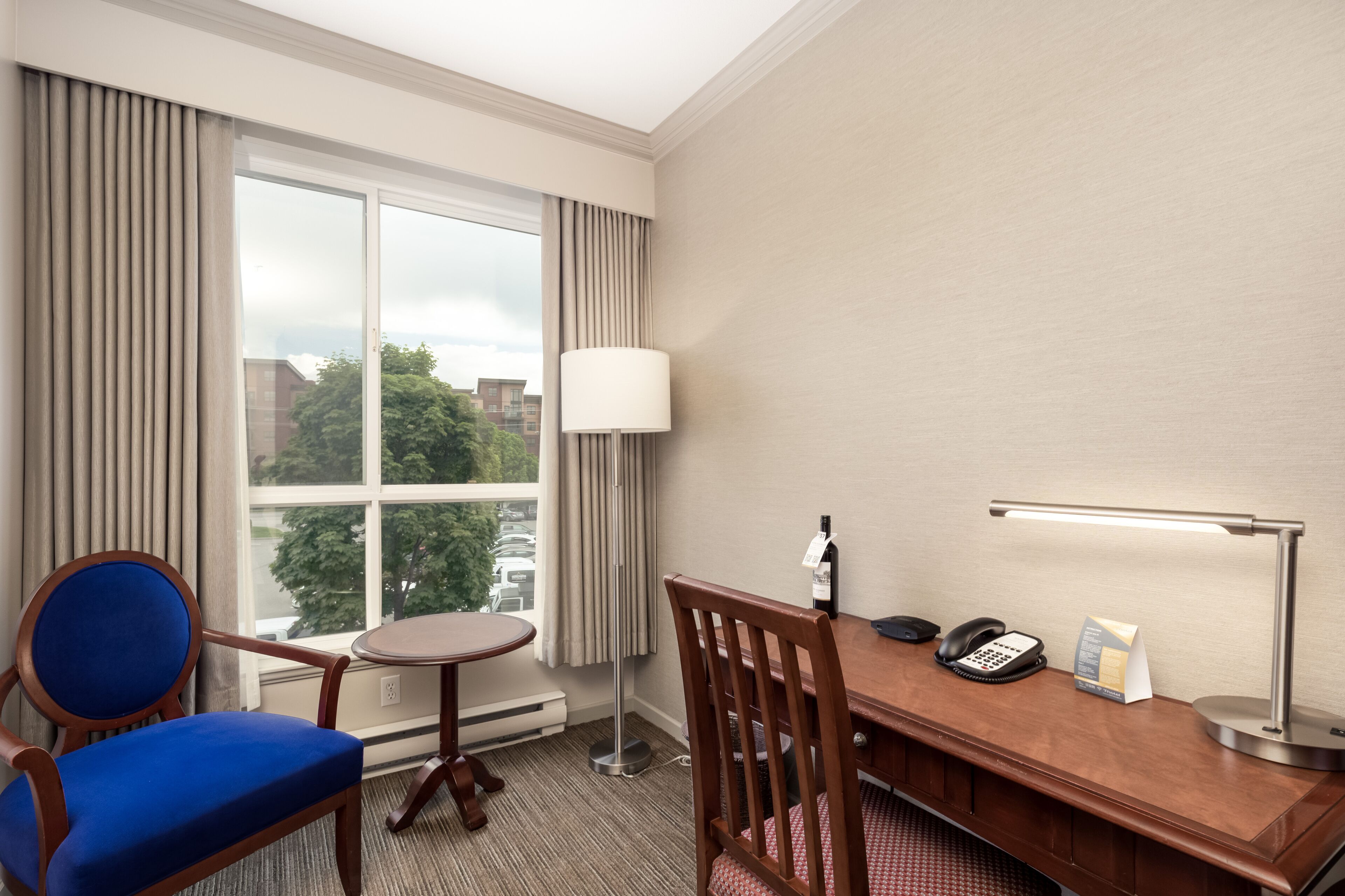Une chambre d’hôtel équipée d’un bureau, d’une chaise, d’une lampe, d’un téléphone et offrant une vue sur la ville par la fenêtre.