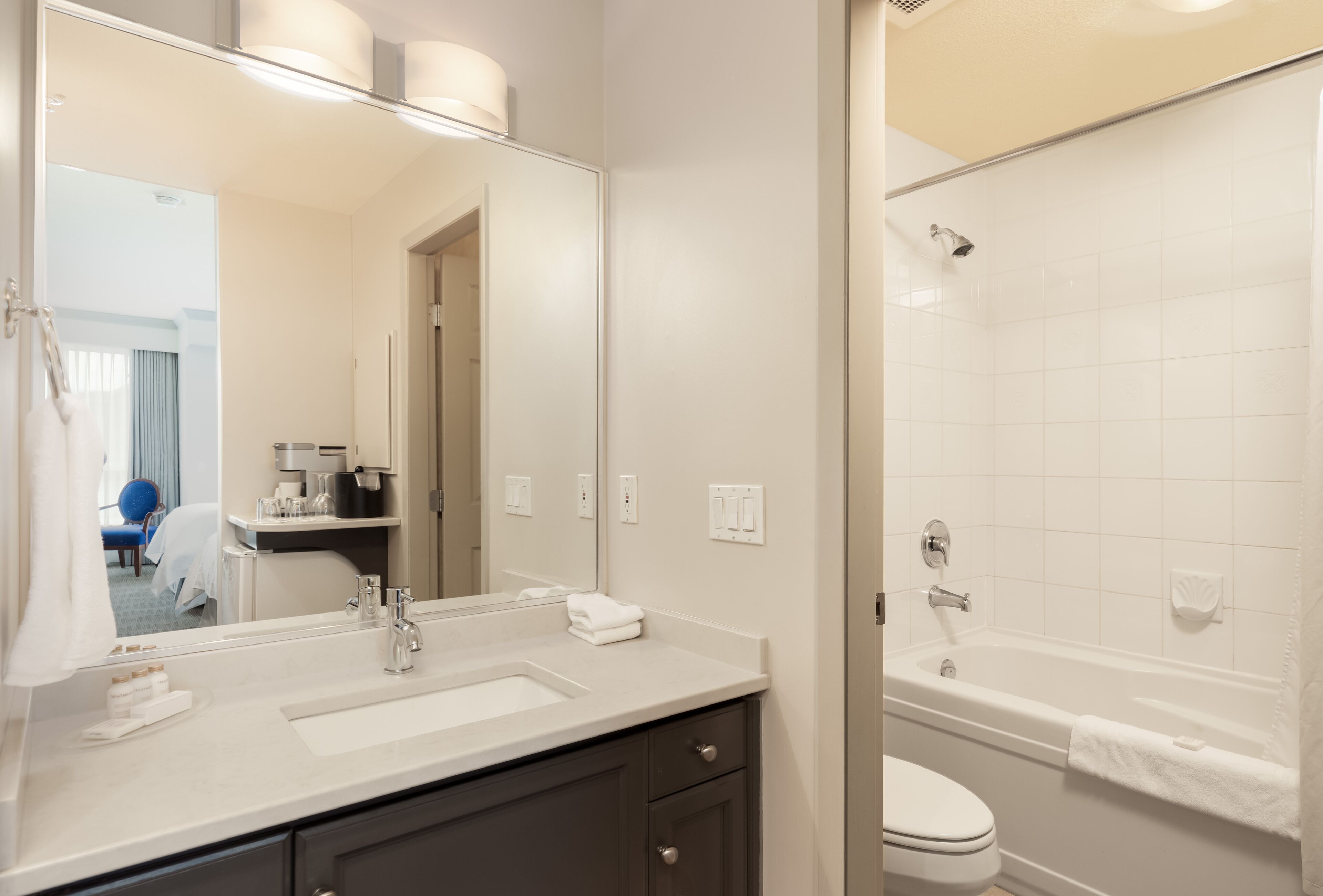 A modern bathroom with a large mirror, two sinks, a toilet, and a bathtub.