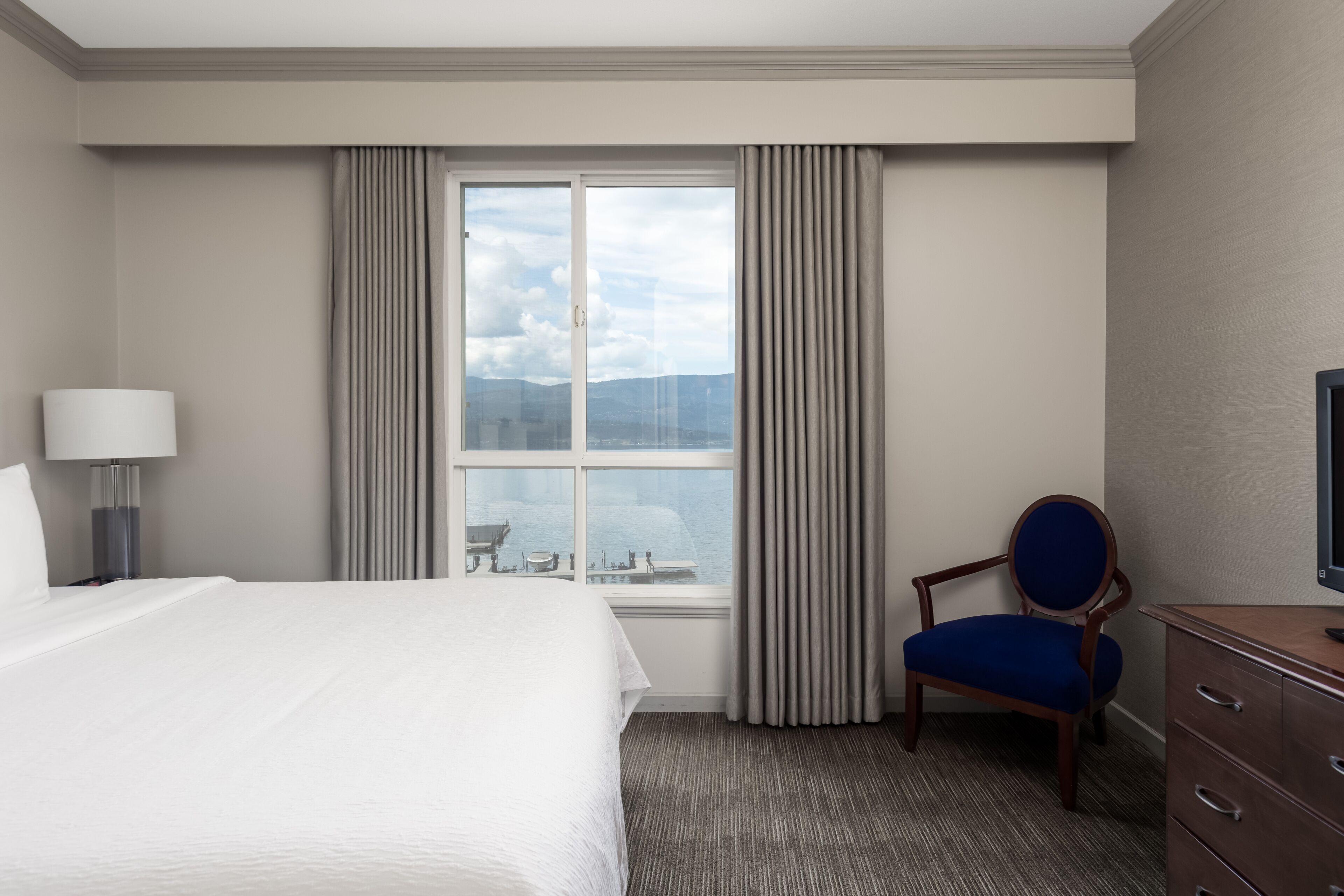 Una habitación de hotel con una cama grande, una silla, un escritorio con televisor y una ventana con cortinas.