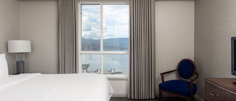 Una habitación de hotel con una cama grande, una silla, un escritorio con televisor y una ventana con cortinas.