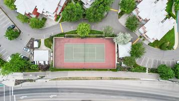 An aerial view of a residential area with a tennis court, multiple houses, and a road.