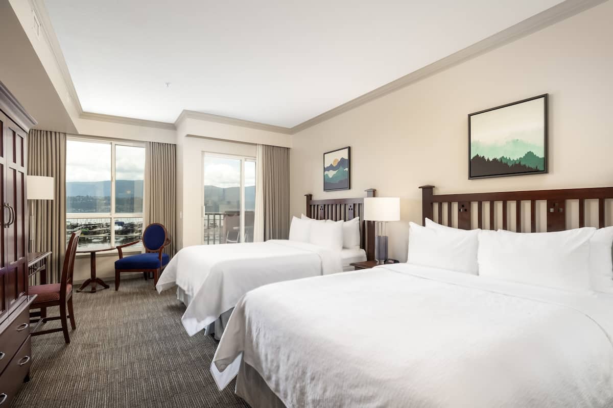 Habitación de hotel con dos camas, un escritorio, una silla y vistas a la ciudad.
