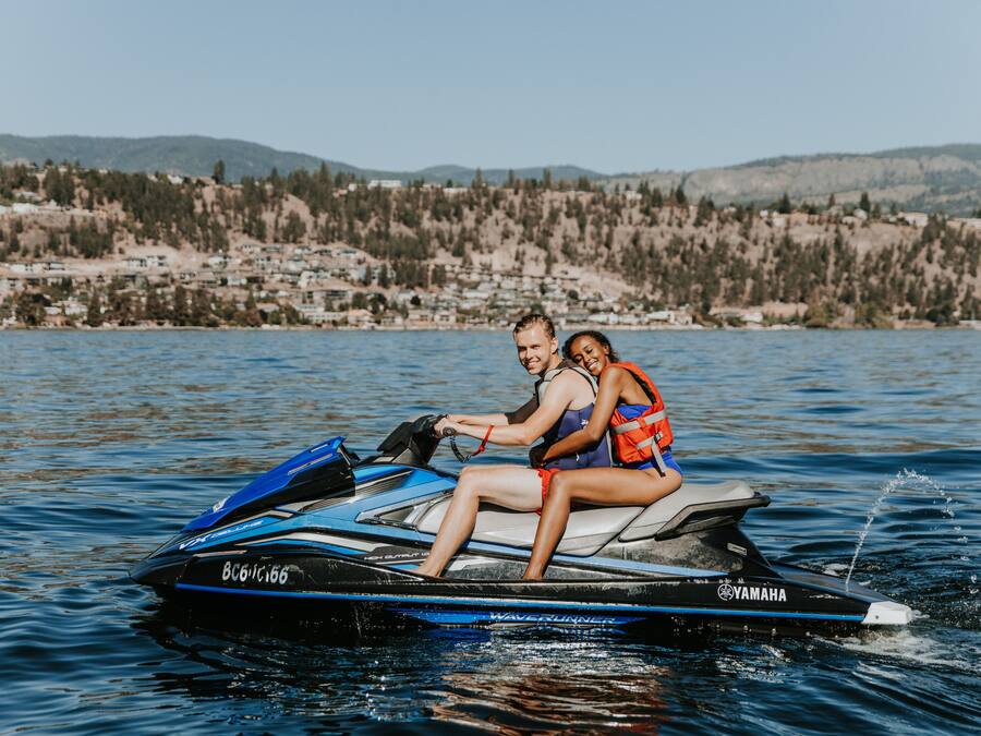 A couple on a Yamaha Waverunner jet ski on a lake with a residential area in the background.