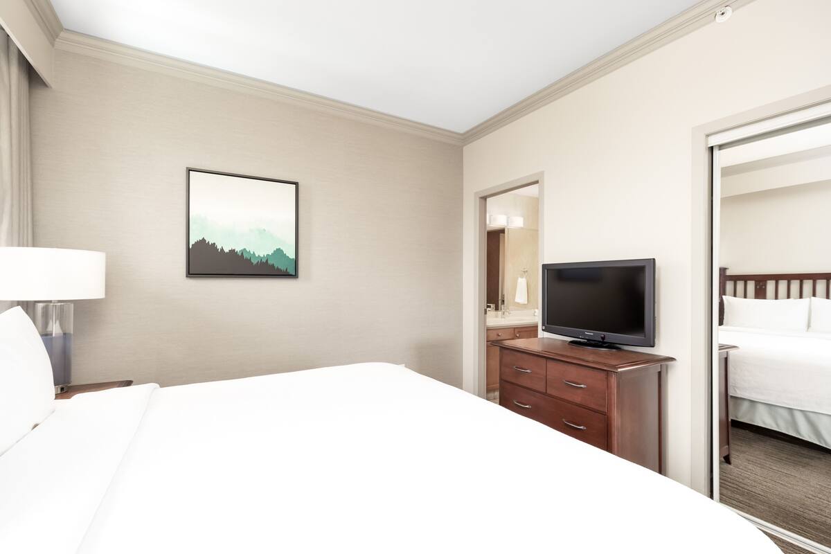 Habitación de hotel con una cama grande, televisión, cómoda y un cuadro en la pared.