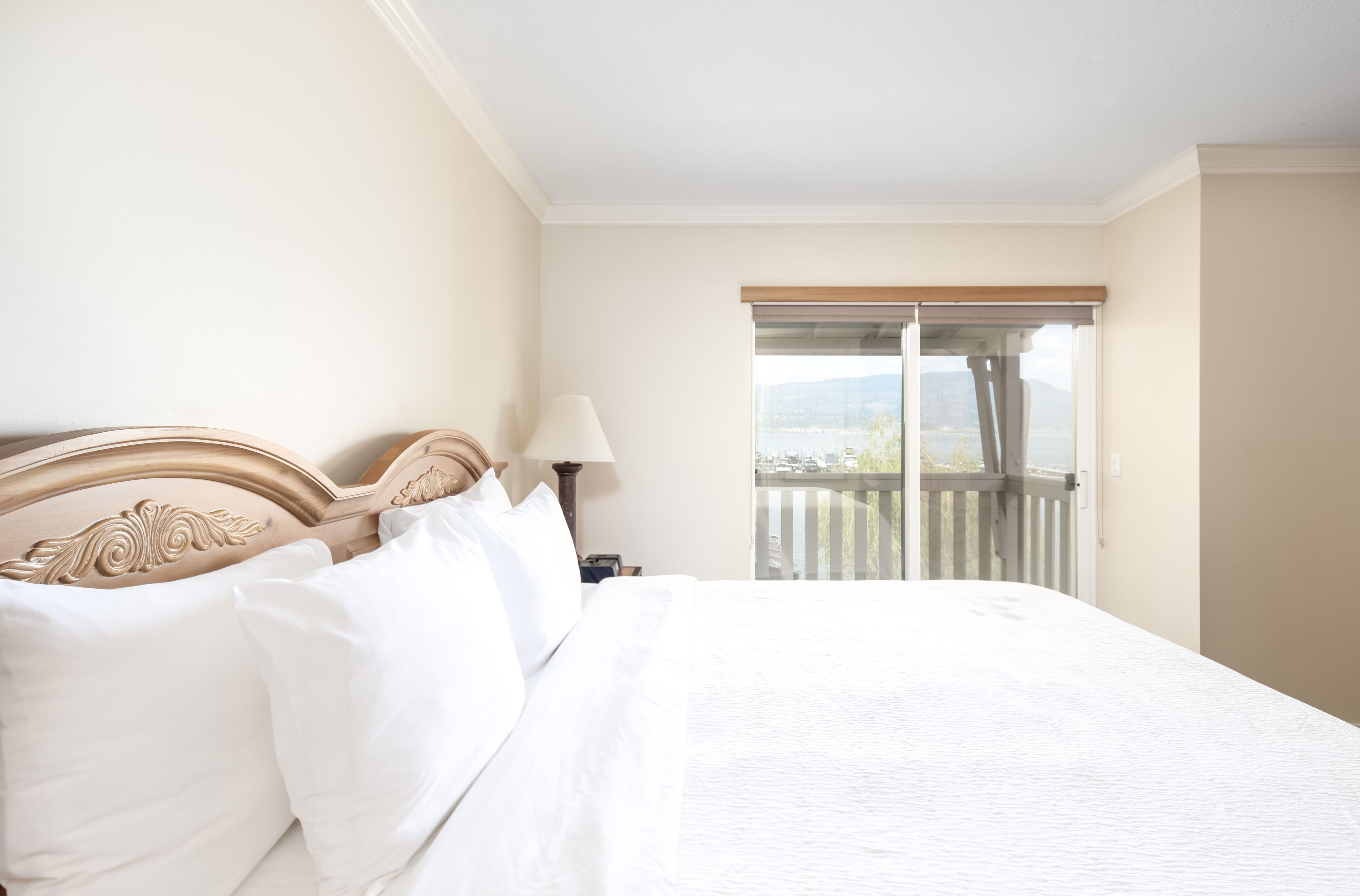 A hotel room with a large bed, a nightstand, a lamp, and a view of a balcony with a railing.