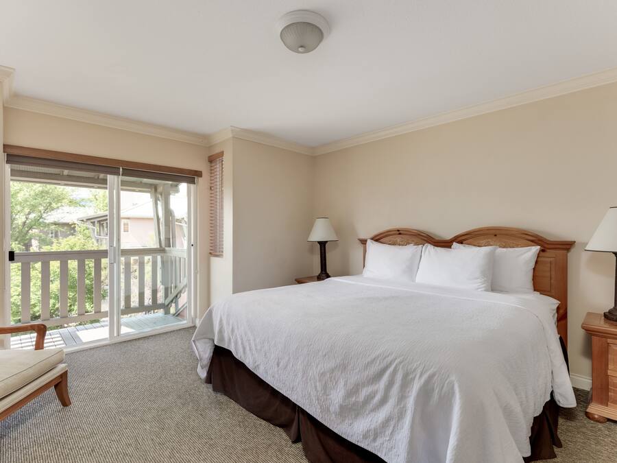 A hotel room with a large bed, two bedside tables with lamps, a chair, and a balcony with a view.