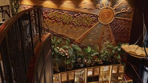 A grand staircase with a wooden railing, a decorative wall with a circular design, and a bar area with various bottles and glasses.