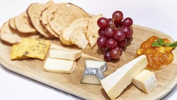 A wooden board with various cheeses, slices of bread, grapes, and a fruit preserve.